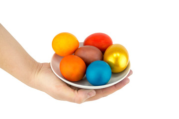Multicolored eggs and golden lie on a ladle in a ceramic saucer on a white background