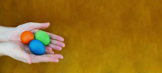 Red blue and green egg lie on the palms of a female hand on a brown wooden background