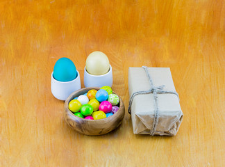 Two eggs pastel color sweet chewing gum in a wooden bowl and gift in kraft paper on a wooden table background
