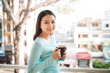Portrait of a happy asian woman thinking and holding coffee or tea cup at breakfast