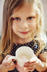 Cute girl holding cup with milk and marshmallow. Childhood concept. 