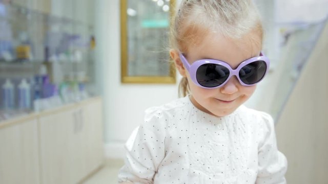 Little Girl tries colorful glasses in medical store - shopping in clinic