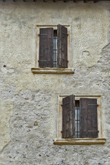 The wall of an old stone house and two windows with shutters.