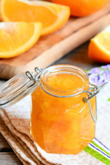 Fototapeta na wymiar Delicious jam made from oranges. Homemade fruit jam in a glass jar, textile napkin, orange slices, wooden board on a table. Useful citrus dessert. Closeup. Vertical photo
