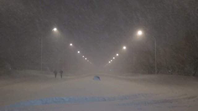 Two people walking down snow covered streets in whiteout blizzard Reykjavik Iceland
