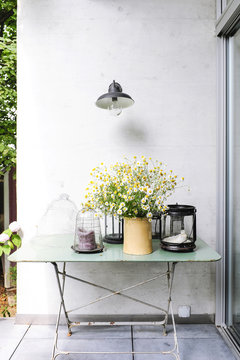 Terrace and metal table with pots, candle holders, chamomile flowers and various flea markets' objects in a vintage atmosphere