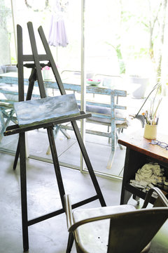 Painter's easel and his blue paint in front of the window of a house