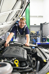 Portrait Automechaniker in der Werkstatt am Motor eines Fahrzeuges // Portrait of car mechanic in...