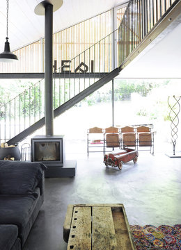 View of the living room of a renovated house with fireplace, waxed concrete floor, blue sofa, garden view and child's car