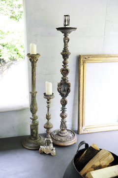 Detail of three golden and antique wooden candlesticks and a gilded frame on a raw concrete wall 