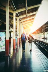 Hipster couple walking on platform at the train station. Two young tourist are ready to get on the train and begin their journey. Travel concept.
