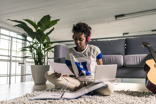 Young woman at home with headphones, laptop and documents next to guitar
