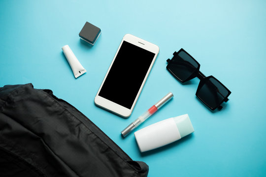 flat lay of black woman bag open out with cosmetics, accessories and smartphone on blue background