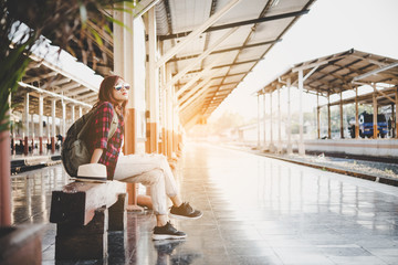 Young hipster woman waiting on bench at train station with backpack. Travel concept.