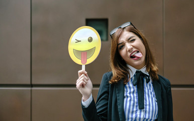 Businesswoman holding emoji smiling with tongue sticking out