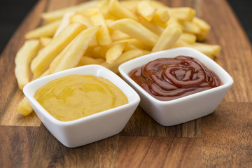 French fries on wooden chopping board with catchup and mustard sauce  