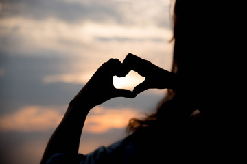 Silhouette hand making heart with sunset