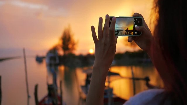 Young Mixed Race Girl Taking Photo of Beautiful Sunset Using Mobile Phone at Fishermans Pier. HD Slowmotion. Thailand.