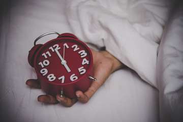 Male hand under blanket reaching out for alarm clock.
