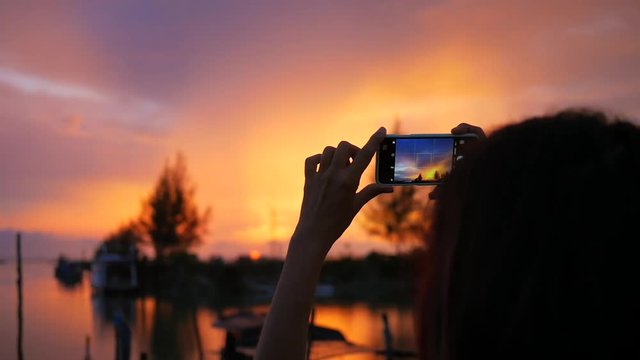 Girl with Long Hair Taking Photo of Beautiful Sunset Using Mobile Phone at Fishermans Pier. HD Slowmotion. Thailand.