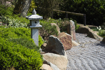 Stone lantern between evergreen plants, rocks and raked gravel, zen garden landscape design in...