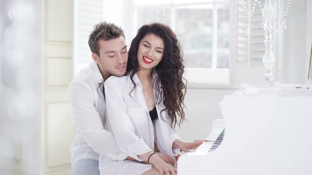  Couple in elegant apartment, woman playing piano in just lingerie & shirt