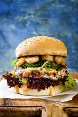 Asian style salmon burger with grilled shrimps, seaweed, lettuce and spicy sriracha mayo sauce served on pieces of brown paper on a rustic wooden board. Bright blue background with copyspace