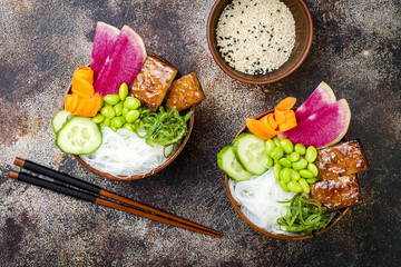 Vegan tofu poke bowls with seaweed, watermelon radish, cucumber, edamame beans and rice noodles. Copy space background, overhead, flat lay