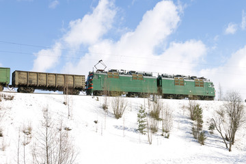 Freight train with electric locomotive moving by railways in winter. Northern Russia, railroad through the snow areas