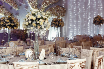 Fototapeta na wymiar luxury wedding decor with flowers and glass vases with jewels on round tables. arrangements of decorations at wedding reception. expensive catering. space for text