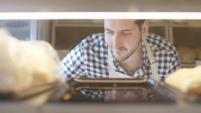  Smiling bakery worker putting pastries onto shelves in display cabinet