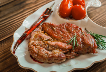 grilled meat with tomato and rosemary on the dish with wooden background