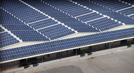There are hundreds of solar panels on the factory's roof. They are standing next to each other.