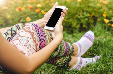 close up white mobile phone in fashionable, trendy woman hands on the background of green grass with flowers during an exercise break