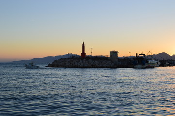 Paisaje marinero ,faro y barca en una puesta de sol en el puerto de Cambrils,Cataluña,Spain.