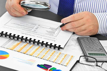 Businessman with pen and magnifying glass, analyzing  financial documents  in the office 
