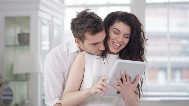  Happy affectionate couple relaxing in apartment & looking at computer tablet