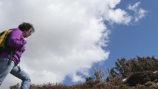 woman hiker with backpack walking a trail in mountains in slow motion