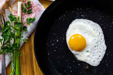 Closeup of fried egg in a black cast-iron pan without oil, sprinkled with salt strag with fresh parsley and garlic. Concept health.