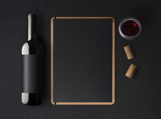 Bottle of red wine with a black label on a dark background, a wine menu template and a glass of...