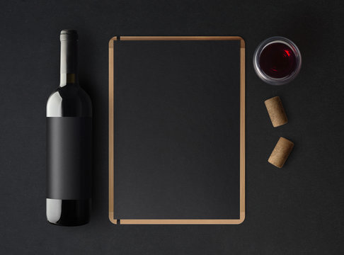 Bottle of red wine with a black label on a dark background, a wine menu template and a glass of wine. Mockup. Top view.