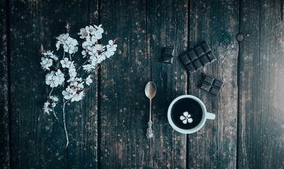 Mug of coffee with chocolate and flowering branches of peach on old wooden.