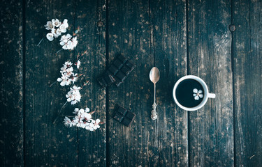 Mug of coffee with chocolate and flowering branches of peach on old wooden.