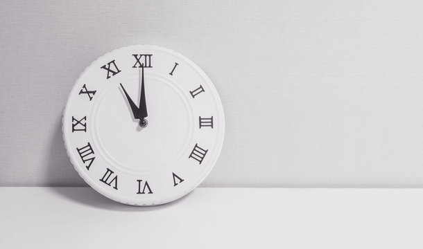 Closeup white clock for decorate in 11 o'clock on white wood desk and wallpaper textured background in black and white tone with copy space