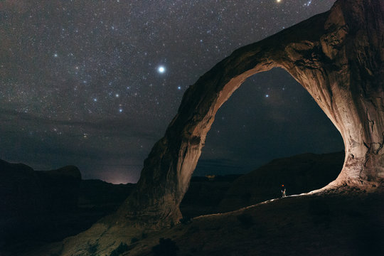 Man standing under the rock formation 
against starry sky