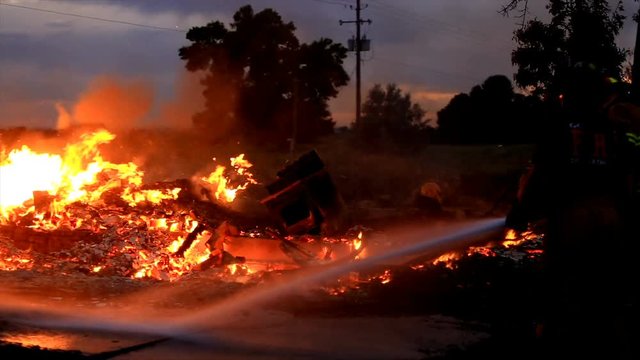 View of fireman spraying hose on fire where house burned down at dusk.