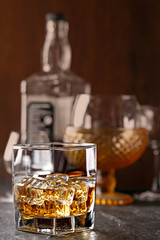 Whiskey glass close-up. Cold with ice, bottle in the background