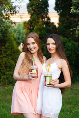 Beautiful young girls in dresses drinking juice in the garden