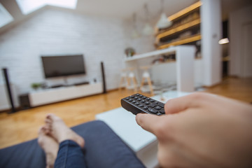 Close up and part of human hand using remote control on sofa in living room