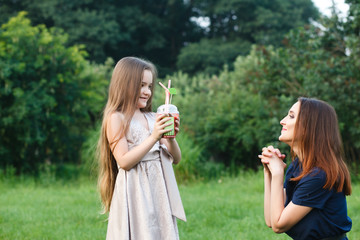 Mom and daughter are walking in a meadow and drinking juice
